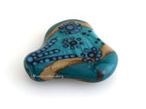 Hearts and Flowers Festive flowers on a mildly-heart shaped focal bead in turquoise, dark sand, black and teal. 30 mm from hole to hole 35 mm at widest point Default Title