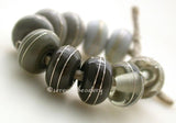 Fine Silver Grays A set of grey colored lampwork beads with 5 different pairs. From top left going counter-clockwise - pearl gray, light gray, dark gray, adamantium, and transparent gray. Each silver wrap is carefully burnished onto the glass bead while it is still hot. Bead Size: 6x11 mm Amount: 10 Beads Hole Size: 2.5 mm Also available in a 7x14 mm size for .00 extra. Glossy,6x11mm,Glossy,7x14mm,Matte,6x11mm,Matte,7x14mm